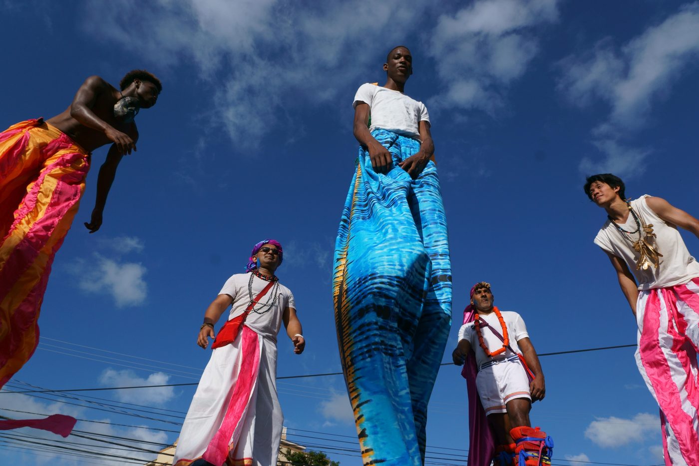 Moko jumbies on stilts against a blue sky
