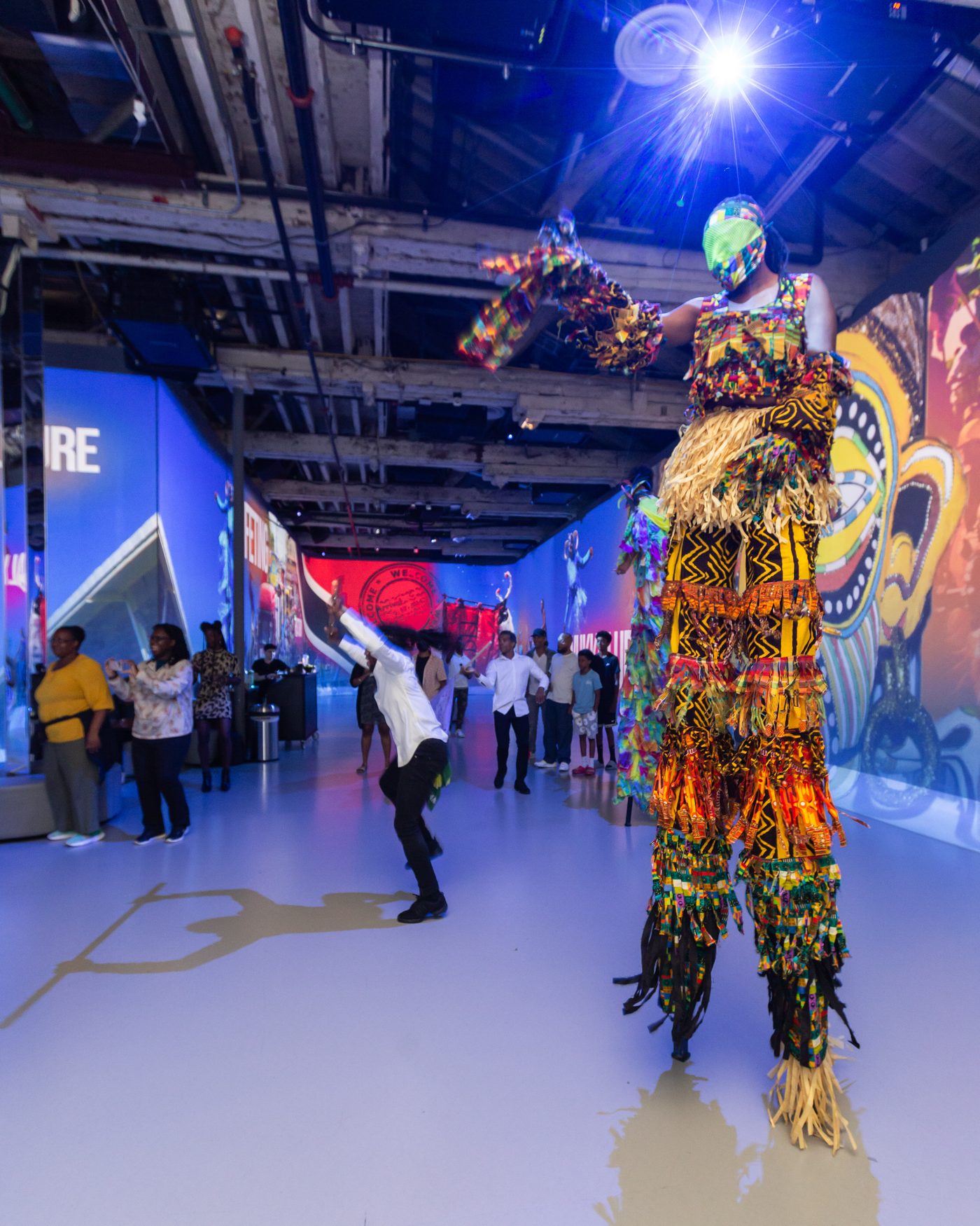 A moko jumbie performing above the crowd inside the immersive venue